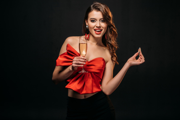 excitada chica de cabello castaño en corsé rojo sosteniendo copa de champán y chips de casino aislados en negro
 - Foto, Imagen