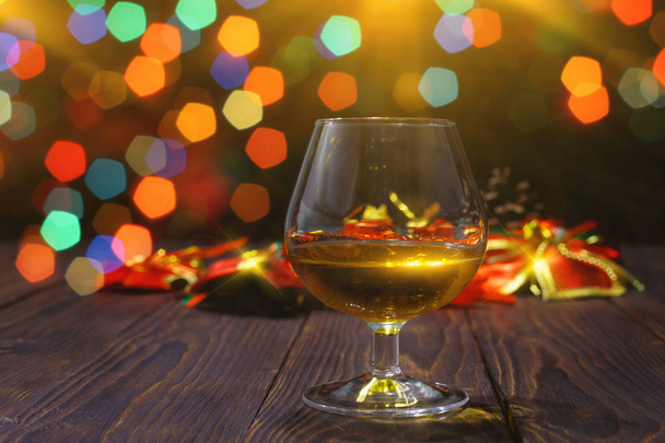 Glass of whiskey or brandy on wooden table on bright glowing background with  beautiful bokeh - Foto, immagini