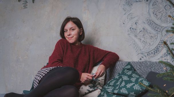 A girl with a short haircut and a warm sweater posing against a gray wall. - Fotó, kép