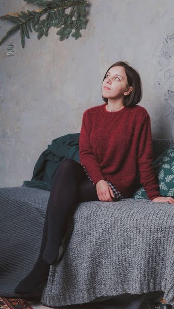Девушка с короткой стрижкой и теплым свитером, позирующим на серой стене
. - Фото, изображение