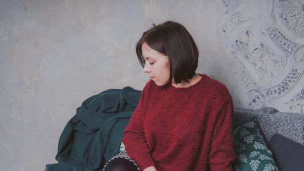 A girl with a short haircut and a warm sweater posing against a gray wall. - Φωτογραφία, εικόνα