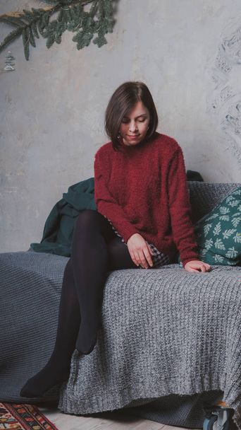 A girl with a short haircut and a warm sweater posing against a gray wall. - Foto, Bild