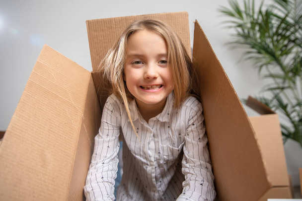 Image of happy girl looking out of cardboard box in apartment - Fotó, kép