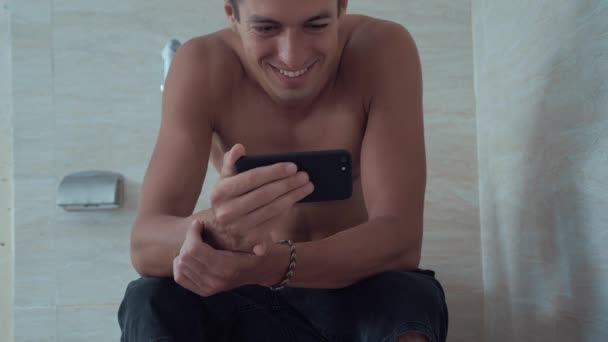 junger Mann benutzt Smartphone auf Toilette zu Hause sitzen. Mann sitzt mit Handy in Toilette. - Filmmaterial, Video