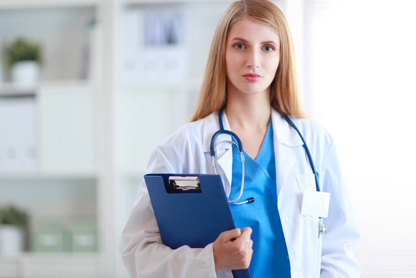 Portrait of woman doctor with stethoscope at hospital corridor, holding a folder. - Fotó, kép