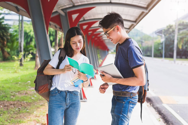 Kaksi aasialaista nuorta opiskelijaa keskustelee kirjan lukemisesta ja kannettavan tietokoneen käyttämisestä tiedon etsimiseen ja oppimiseen. Koulutuksen ja ystävyyden käsite. Onnellisuus ja oppiminen käsite. Ystävät ja ystävät teema
. - Valokuva, kuva