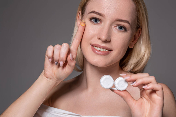 Portrait of young beautiful woman with natural makeup and contact eye lens in hand. Close-up of female model holding white lens box. - Valokuva, kuva
