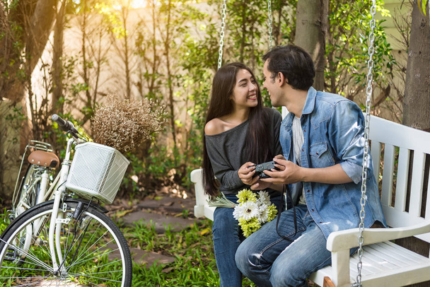 Aziatische paar hebben oog contact als romantische moment bij Bank in natuurpark met fiets. Mensen en levensstijlen concept voor Valentijnsdag en huwelijksceremonie. Liefde op het eerste gezicht thema. - Foto, afbeelding