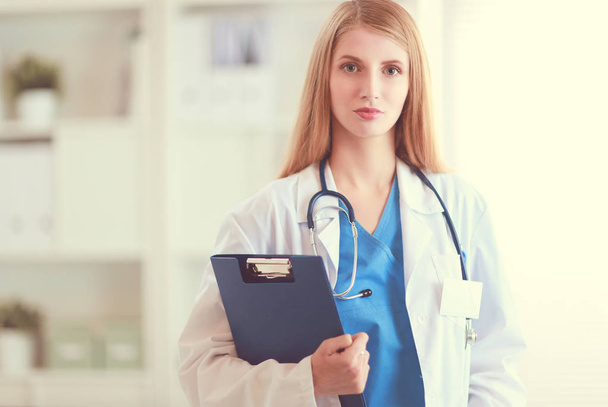 Portrait of woman doctor with stethoscope at hospital corridor, holding a folder. - Valokuva, kuva