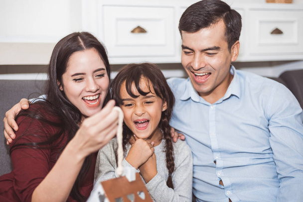 Father and mother surprise their daughter by gift or new toy. Parents and children are happy together in home on sofa in living room. Family and Happiness of life concept. - Photo, Image