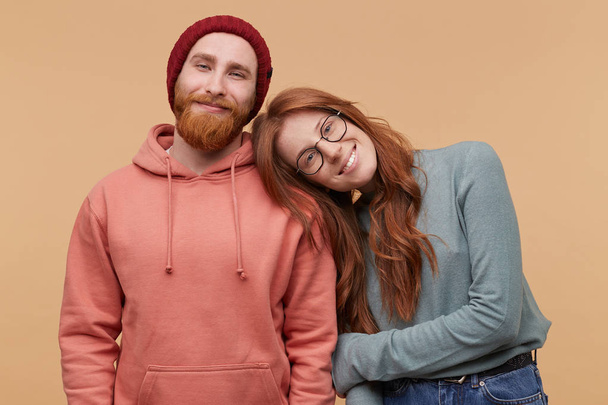 Indoor shot of cheerful redhead woman, keeps her hand on boyfriend shoulder, smiles and feels happy. family album image of Caucasian couple enjoy their partnership. Isolated over biege background - 写真・画像