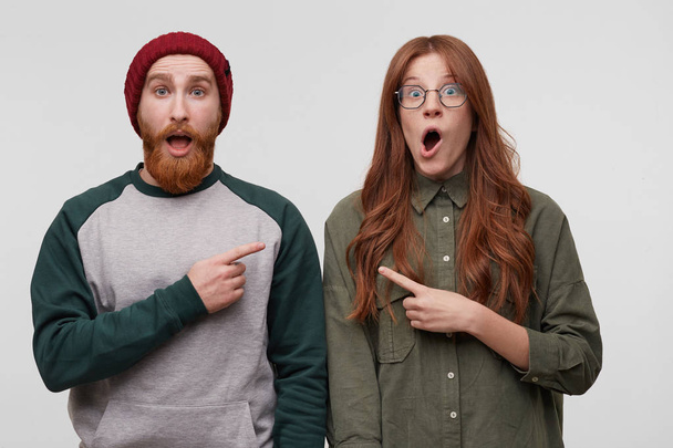 Family portrait of shocked and stunned couple, indicates each other with four finger and keep their mouth open widely. Isolated over white studio wall - Foto, Imagem