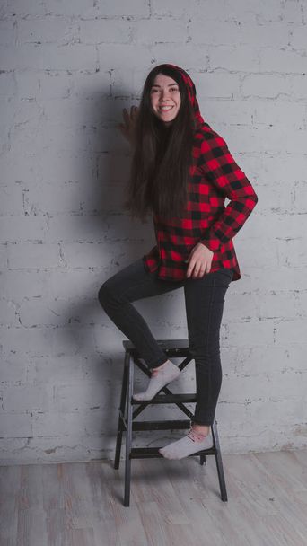 The girl in the red black plaid shirt. Brunette posing with a chair, against a brick wall. Beautiful woman on grey background.  - Fotó, kép