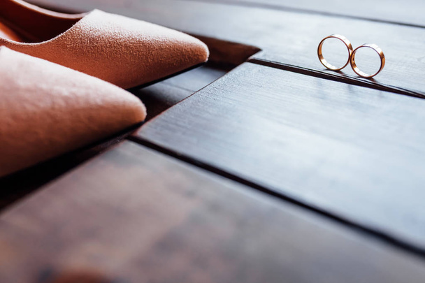 Sapatos bege clássicos elegantes da noiva, dois anéis de casamento estão em um fundo de madeira
 - Foto, Imagem