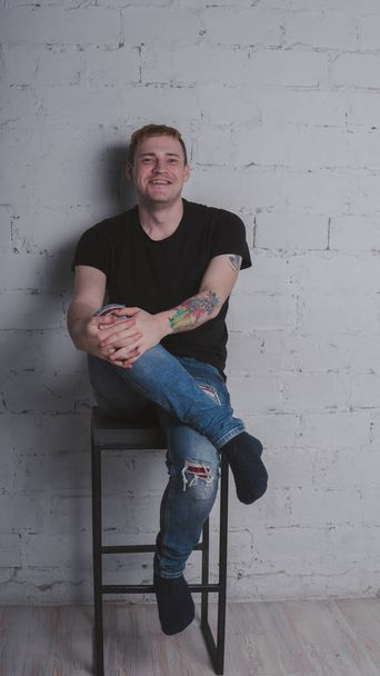 Egy jóképű férfi egy fekete póló, szürke tégla fal. Brutális srác egy tetoválás - Fotó, kép