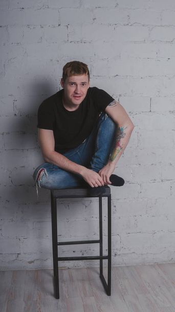 A handsome man in a black t-shirt, against a gray brick wall. Brutal guy with a tattoo - Foto, Bild