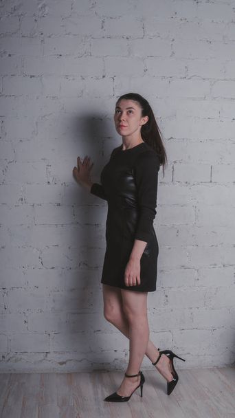 Mädchen posiert vor einer weißen Backsteinwand. Modell in schwarzem Kleid. brünett östliches Aussehen. - Foto, Bild