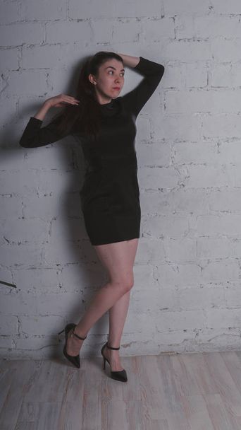 Girl posing against a white brick wall. Model in black dress. Brunette Eastern looks. - Fotoğraf, Görsel