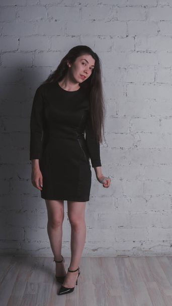 Girl posing against a white brick wall. Model in black dress. Brunette Eastern looks. - Zdjęcie, obraz