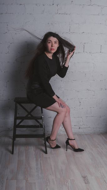 Girl posing against a white brick wall. Model in black dress. Brunette Eastern looks. - Foto, imagen