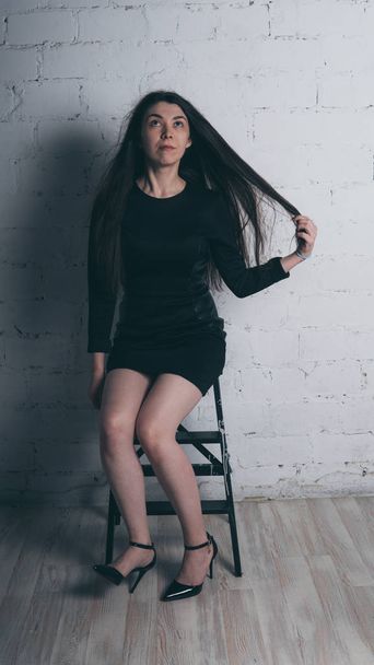 Girl posing against a white brick wall. Model in black dress. Brunette Eastern looks. - Fotó, kép