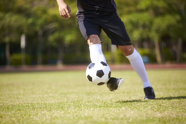 κοντινή λήψη ενός πόδια της Ασίας ποδοσφαιριστής που χειρίζονται την μπάλα στο γήπεδο ποδοσφαίρου. - Φωτογραφία, εικόνα
