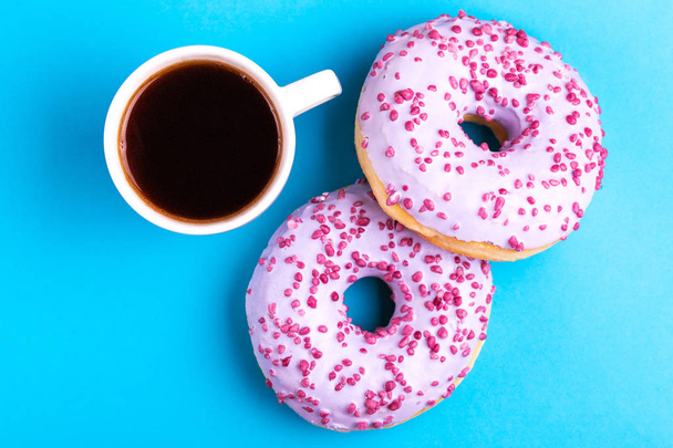 Two tasty lilac donuts with sprinkle and cup of strong coffee on bright blue background. Unhealthy, but delicious sweets. Copy space. Top view - Photo, image