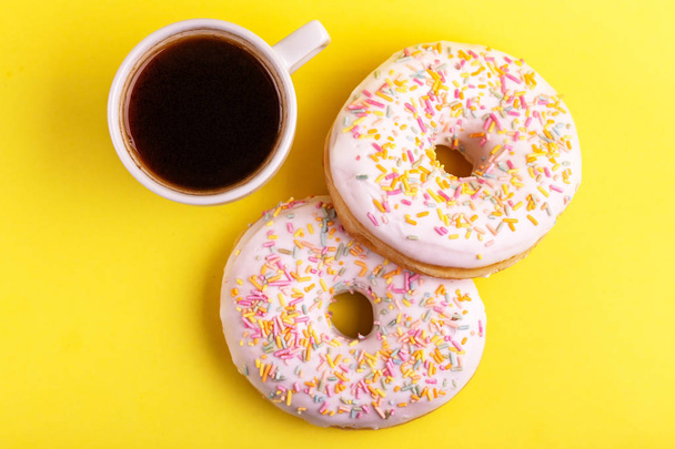 Two delicious vanilla donuts with sprinkle and cup of coffee on bright yellow background. Unhealthy, but tasty sweets. Copy space. Top view - Φωτογραφία, εικόνα