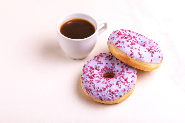 Two delicious lilac donuts with sprinkle and cup of coffee on light marble background. Unhealthy, but tasty sweets. Copy space. Horizontal view - Foto, immagini