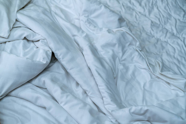 White linen blanket in hotel bedroom. Close up detail of messy white blanket after waking up in morning. Comfortable bed with soft white duvet. Sleep tight with good quality bedding household concept. - Photo, image