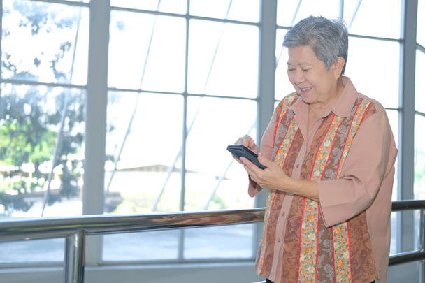 cep telefonu terasta tutan Asya yaşlı kadın. Yaşlı kadın verandada Smartphone kullanarak. cep telefonu ile üst düzey manifatura mesaj - Fotoğraf, Görsel