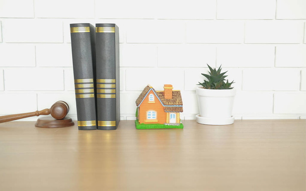 δικαστής βιβλίο νόμου σφυρί & σπίτι σπίτι μοντέλο σε ξύλινο γραφείο κοντά σε λευκό τοίχο. ακίνητη περιουσία διαφοράς & ιδιότητα δημοπρασία έννοια - Φωτογραφία, εικόνα