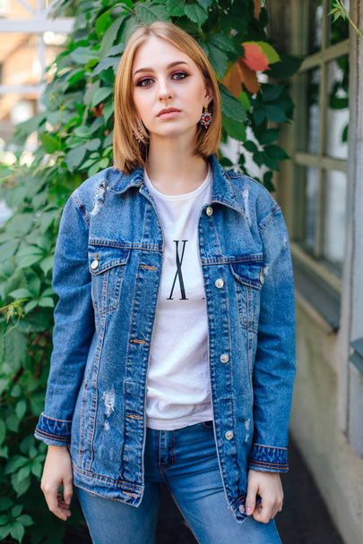 Fashion girl standing outdoors in denim oversized jacket and beautiful ear rings. - Фото, зображення