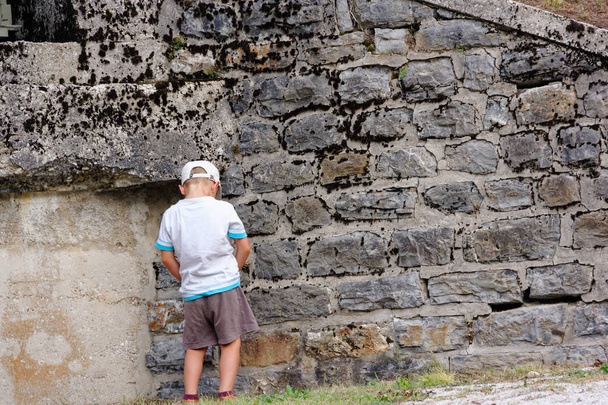chico meando en una pared de piedra en la ciudad
 - Foto, Imagen
