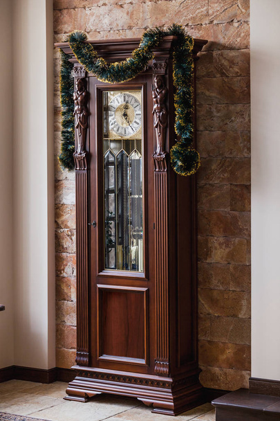 Clock High floor in a brown wooden carved case decorated with a New Year's garlan - Foto, immagini