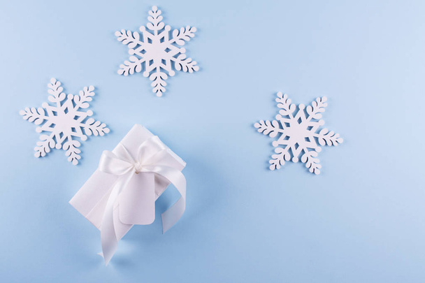 Secret Santa kerst spel. Cadeau-uitwisseling. Witte geschenkdoos met opmerking sneeuwvlokken op blauwe pastel achtergrond bovenaanzicht copyspace verpakt.  - Foto, afbeelding