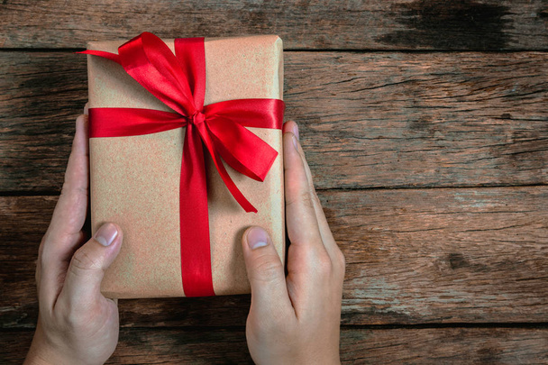 bónusz emberi ember kézzel ad a jelenlegi barna ajándék doboz csokornyakkendő piros szalag a régi fa padló tetején Nézd kellemes karácsonyi ünnepeket és boldog új évet koncepció - Fotó, kép