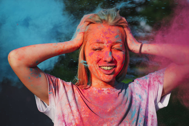 Adorable blonde girl having fun with exploding blue and pink dry powder celebrating Holi festival - Foto, afbeelding