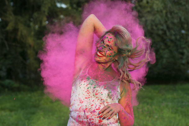 Porträt einer glücklichen jungen Frau, die Spaß in einer Wolke aus rosa trockener Holi-Farbe im Park hat - Foto, Bild
