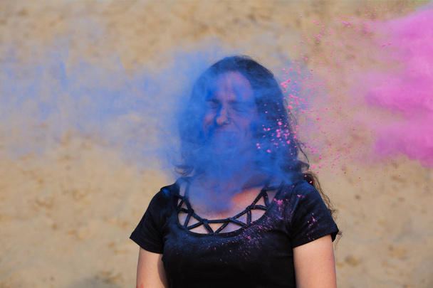 Piękny model młody pozowanie z wybuchające wokół jej fioletowy i niebieski proszek Holi w pustyni - Zdjęcie, obraz