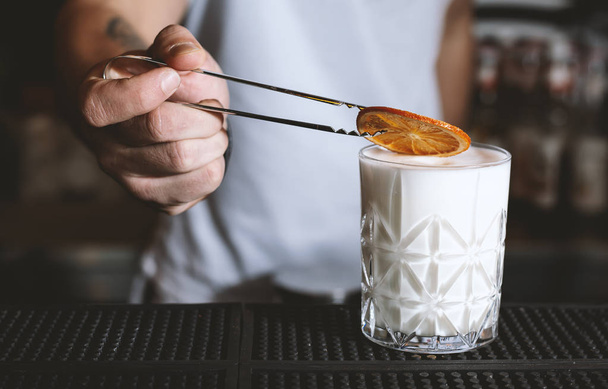 Бармен наливает алкогольный молочный коктейль из шейкера в коктейльный бокал на барной стойке
 - Фото, изображение