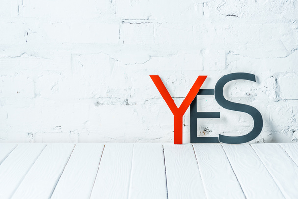 "yes" lettering with decorative red and black letters on wooden table near white brick wall - Foto, immagini