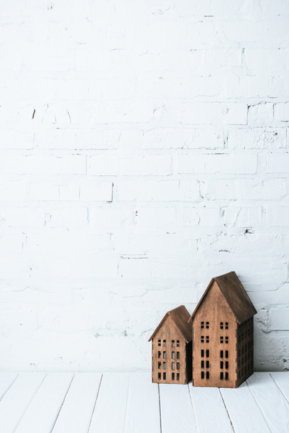 деревенские модели домов на деревянном столе возле стены из белого кирпича
 - Фото, изображение
