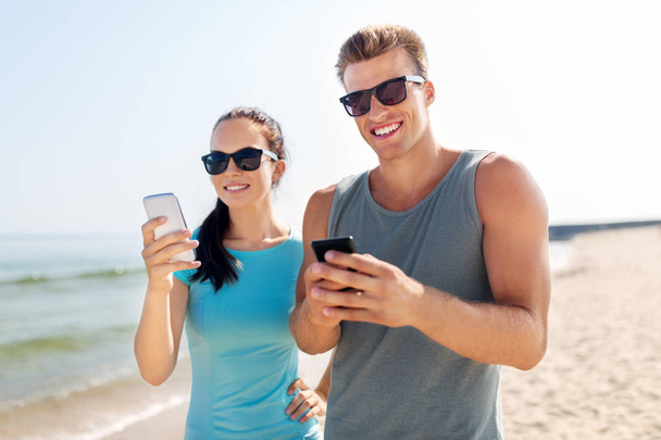couple in sports clothes with smartphones on beach - Φωτογραφία, εικόνα