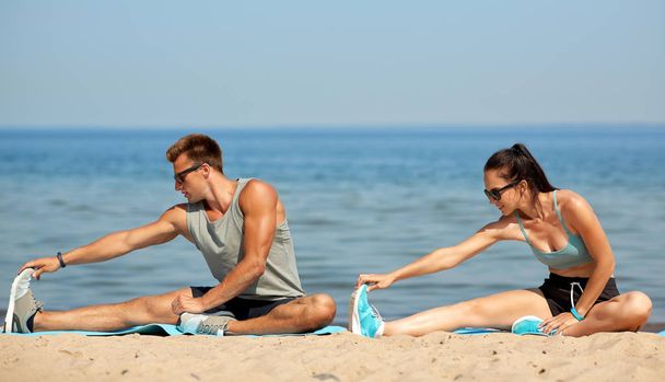 gelukkige paar stretching benen op strand - Foto, afbeelding