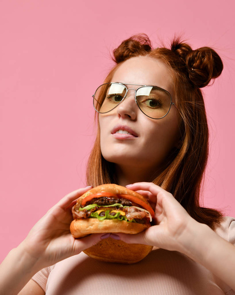 Close up portrait of a hungry young woman eating burger isolated over pink background - Valokuva, kuva