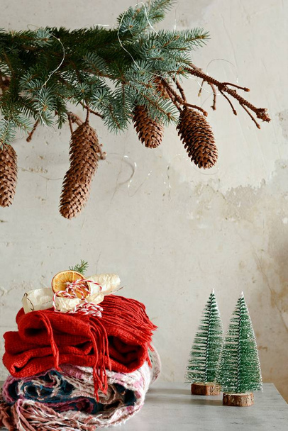 テーブルの上の暖かい服の山。家の中のクリスマスの雰囲気。部屋コーンのモミの枝で装飾。ライフ スタイル。秋や冬の静物。ホームの雰囲気、冬の服. - 写真・画像
