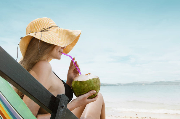 Frau sitzt auf Liege und trinkt Cocktail aus Kokosnuss - Foto, Bild