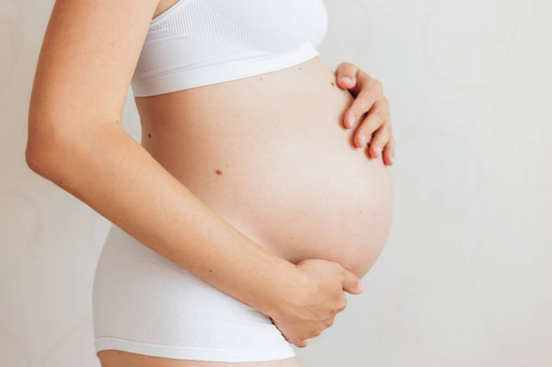 Беременная женщина со многими родимыми пятнами (невус) в белом нижнем белье. Молодая женщина ждет ребенка
. - Фото, изображение