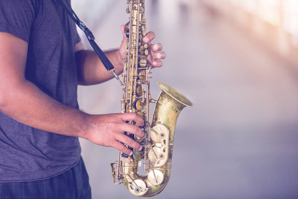 A street musician plays the saxophone with blurry people walking on skywalk in city. - Zdjęcie, obraz